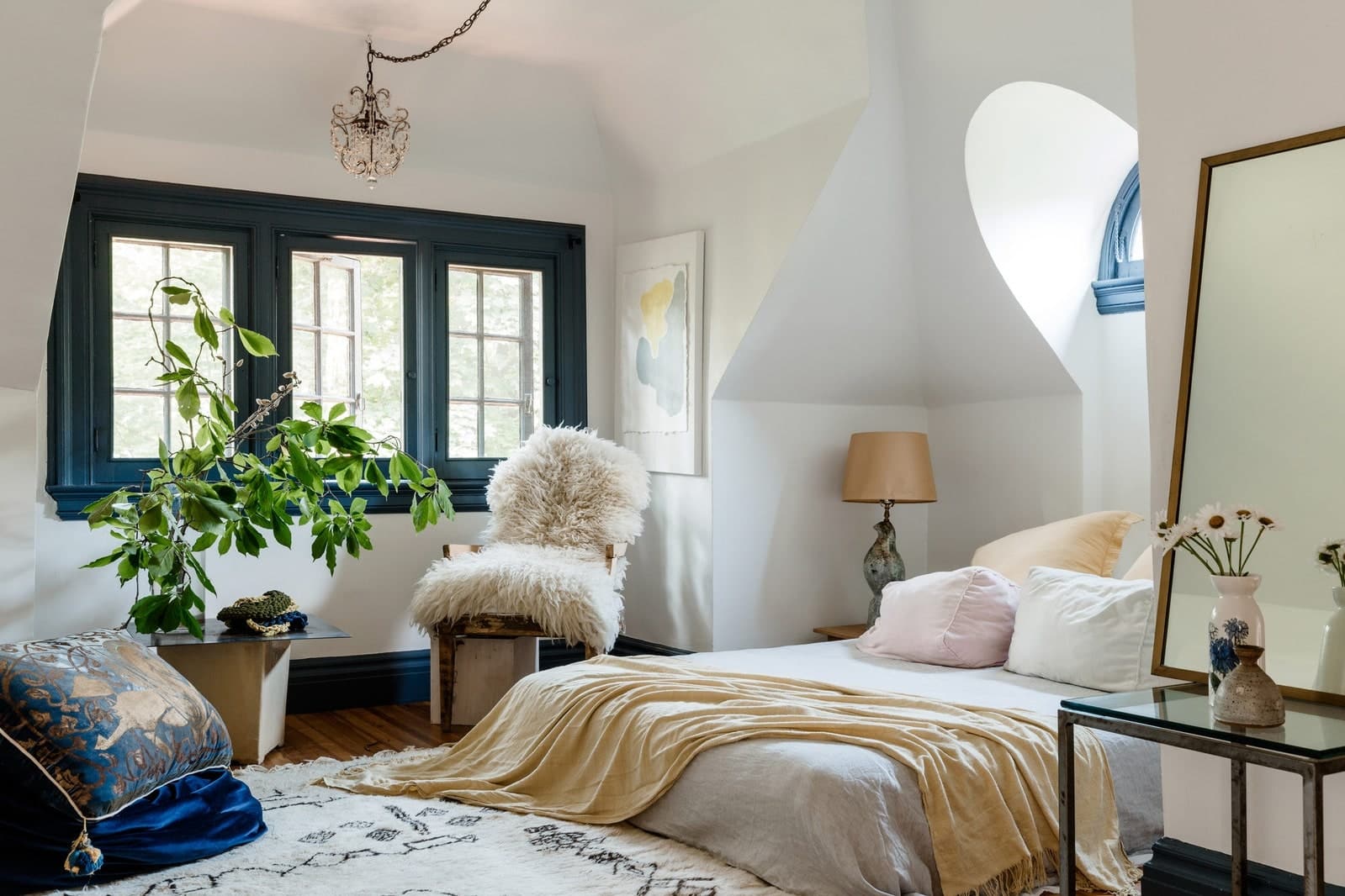 The bright, richly decorated bedroom of an AirBnB with white walls, dark wood floors, decorative rug, and exotic plant.